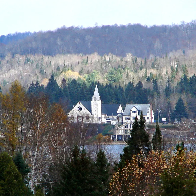 Église blanche au bord du lac à Lac-des-Plages, en fin d'automne, entourée de conifères et de collines boisées