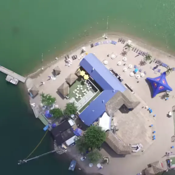 Vue aérienne de la pointe sablonneuse de Pointe-Calumet sur le lac des Deux Montagnes : plage, quai et bâtiments à toit bleu entourés d'eau verte
